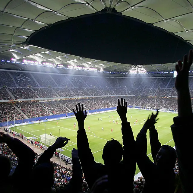Fotballbane og tribune, med skygge av supportere som jubler