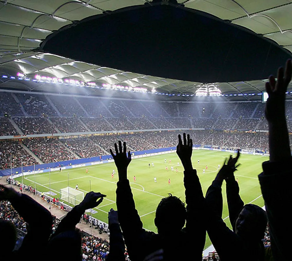 Fotballbane og tribune, med skygge av supportere som jubler
