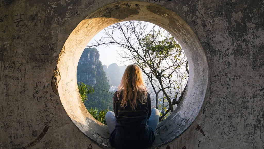 Kvinne sitter i en sirkelformet statue og stirrer ut i et landskap
