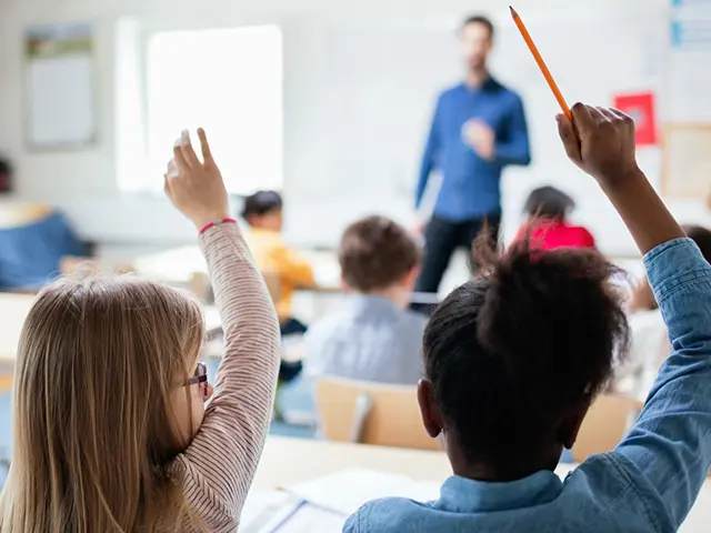 To barn som rekker opp hånden i et klasserom