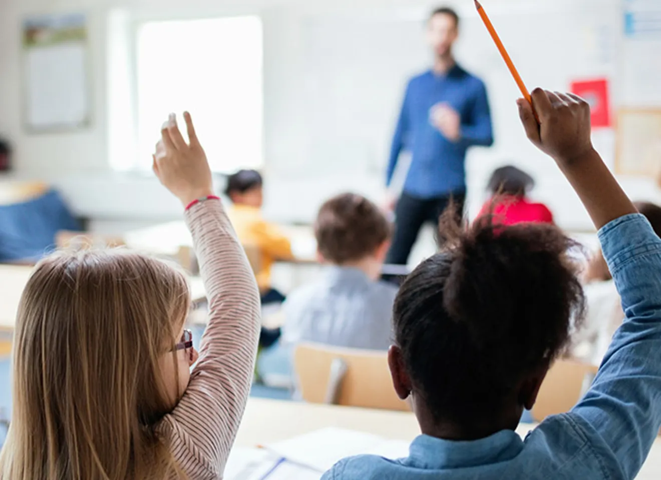 To barn som rekker opp hånden i et klasserom