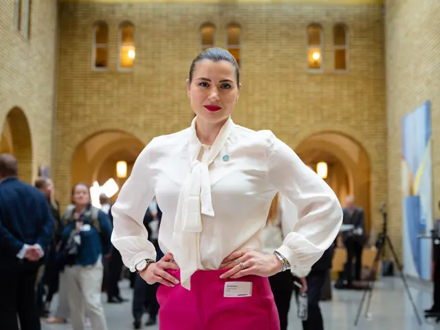 Elisabet haugsbø i vandrehallen på Stortinget, hvit bluse, rosa bukse, med armene i siden, bestemt ansiktsuttrykk