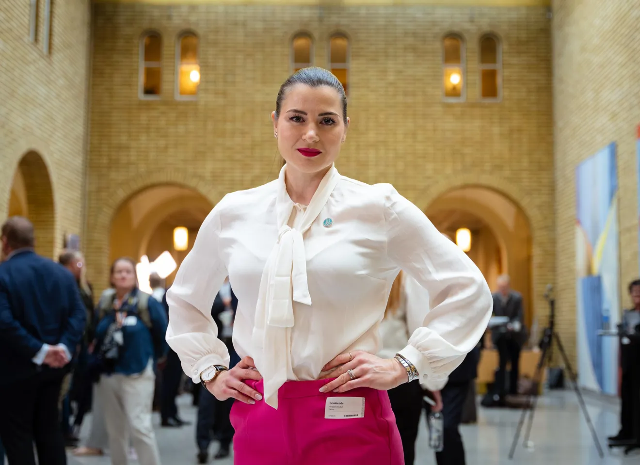 Elisabet haugsbø i vandrehallen på Stortinget, hvit bluse, rosa bukse, med armene i siden, bestemt ansiktsuttrykk