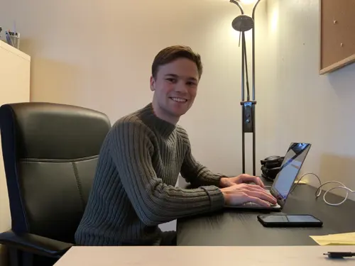 Erlend Hermansen med laptop på hjemmekontor smiler til kamera