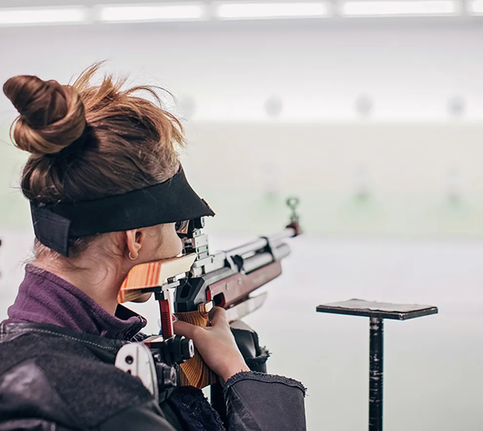 Ung kvinne sikter med gevær på skytebane