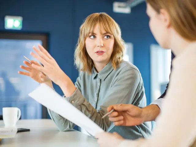 Kvinne ser på en annen kvinne og forklarer noe med tydelige håndbevegelser