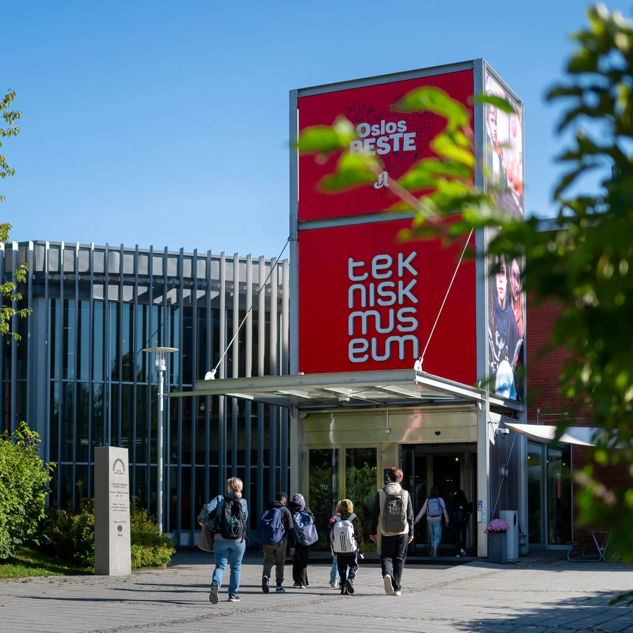 Inngangen på Teknisk museum i Oslo, blå himmel, barn som går med ryggen til mot inngangen 