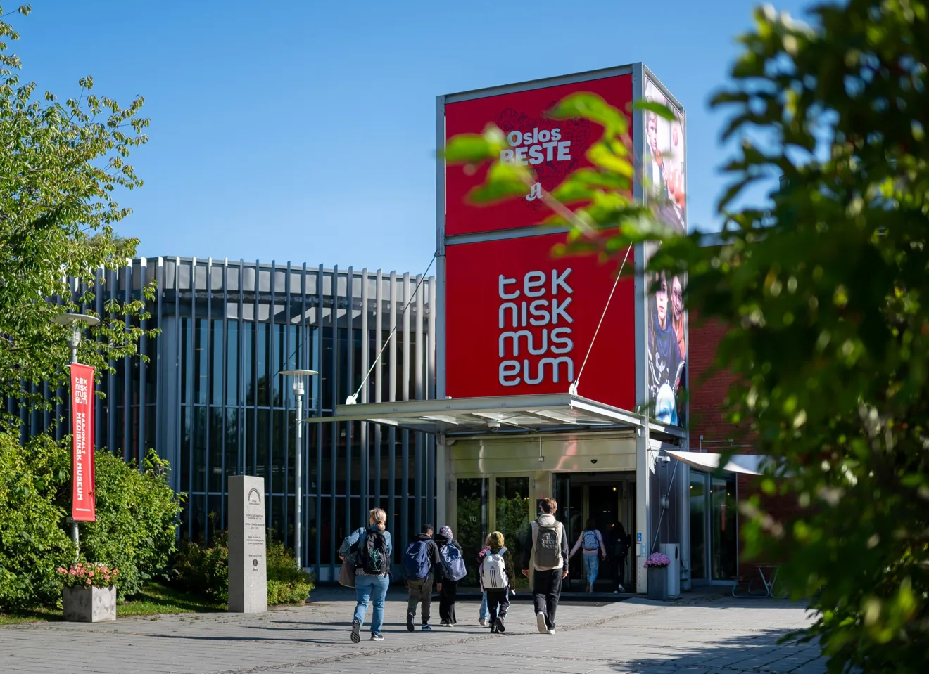 Inngangen på Teknisk museum i Oslo, blå himmel, barn som går med ryggen til mot inngangen