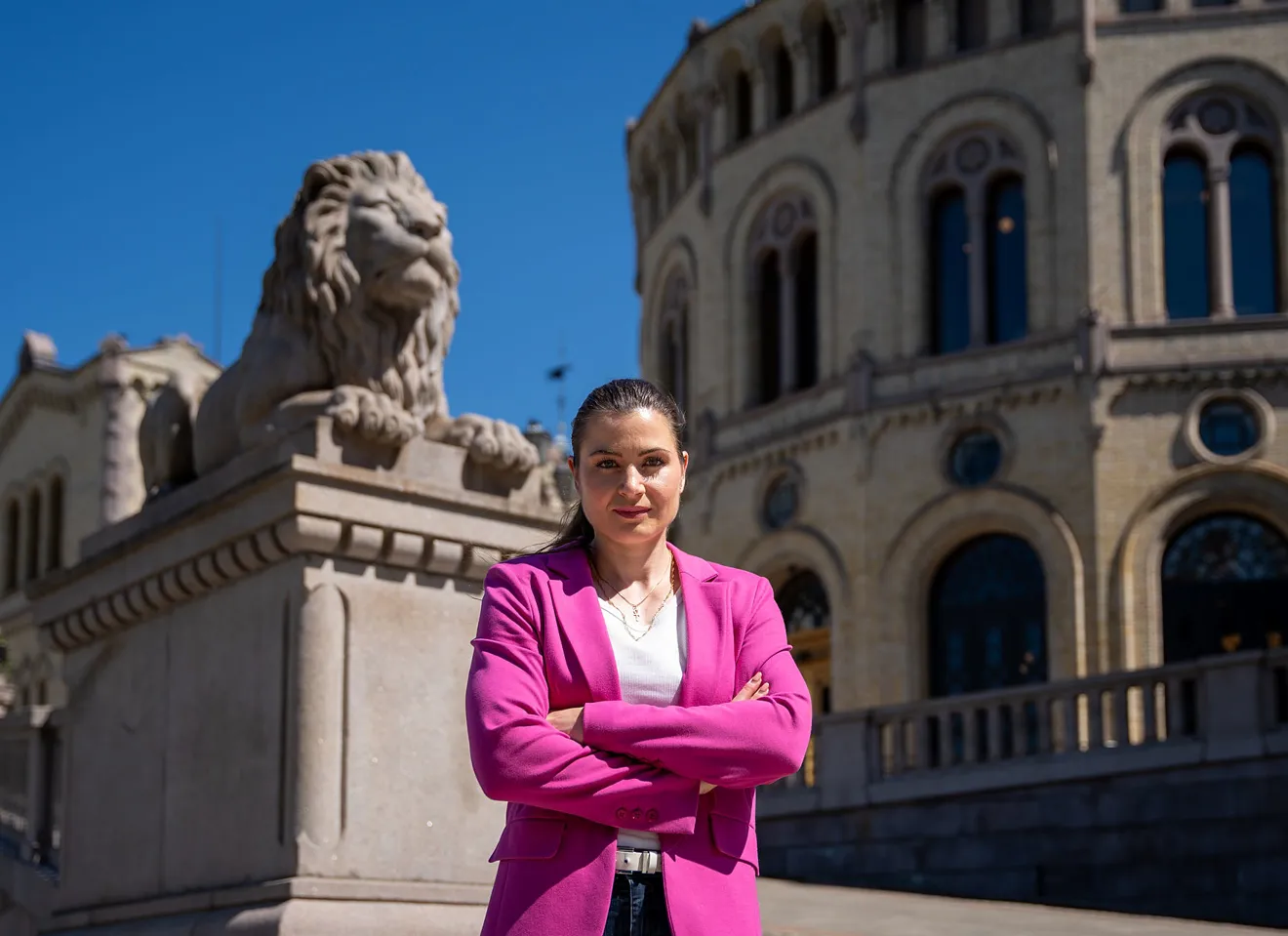 Elisabet Haugsbø med rosa dressjakke foran Stortinget. blå himmel. alvorlig ansiktsuttrykk