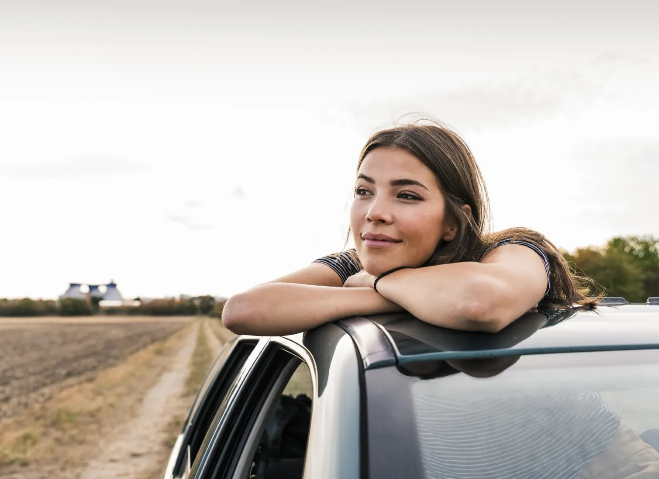 Kvinne som lener seg ut av solvinduet på en bil og ser ut i horisonten med et smil