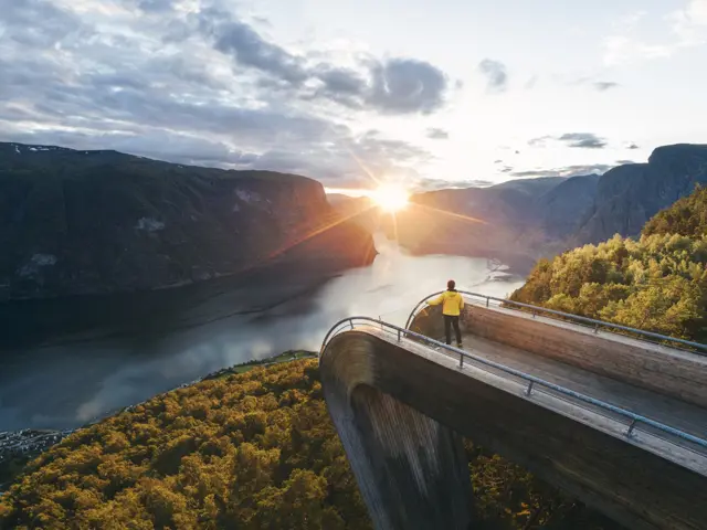 En kvinne stående på et usiktspunkt på en fjelltop i solnedgang