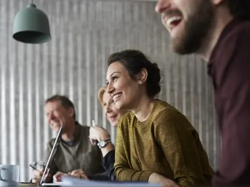 Illustrasjonsbilde av flere ansatte rundt et bord, en kvinne i fokus som smiler