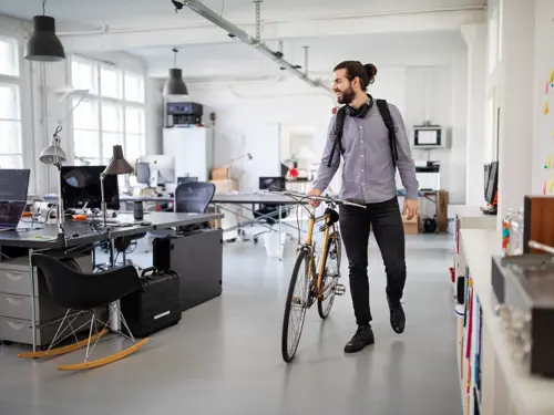 En smilende person går gjennom et kontorlokale med en sykkel.