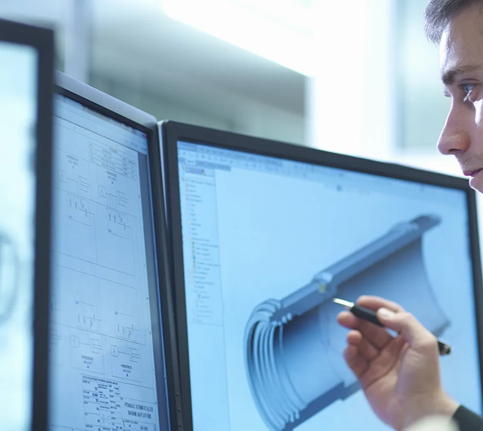 En ung mann foran flere dataskjermer med 3D CAD-tegninger