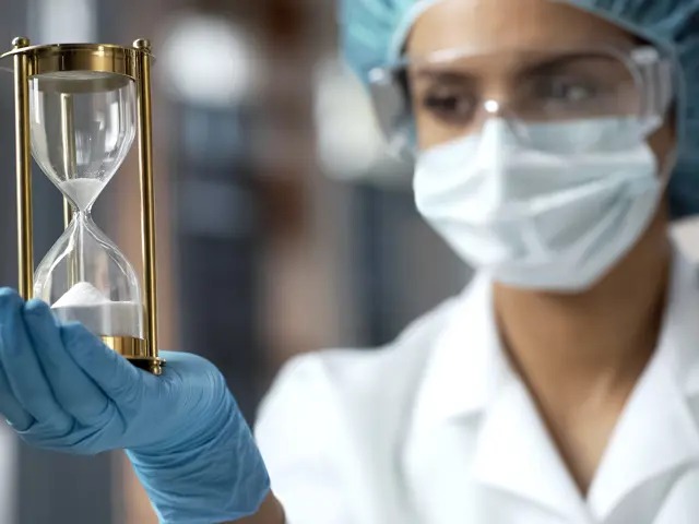 Illustrasjonsbilde av en kvinnelig forsker i verneutstyr som holder en timeglass