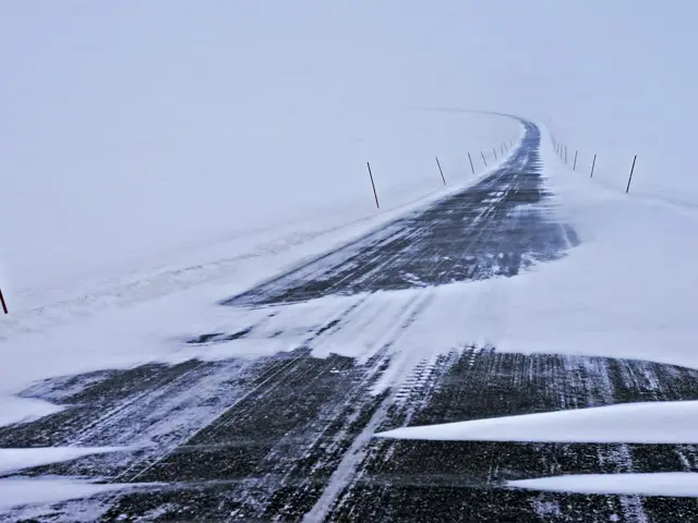 En nesten snødekket vei i en øde vinterlandskap med mye tåke