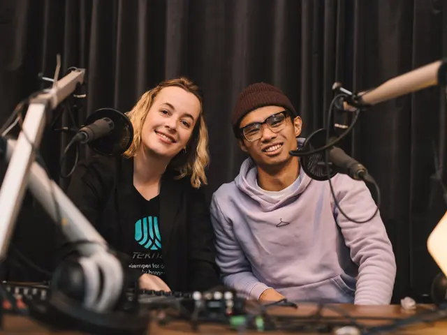 To programledere foran mikrofoner smiler til kamera