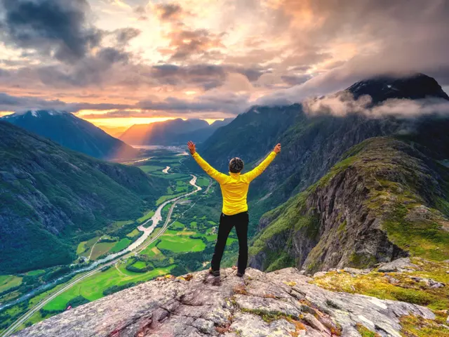 Illustrasjonsbilde av en kvinne opp på en fjelltop og ser utover en fjord i solnedgang