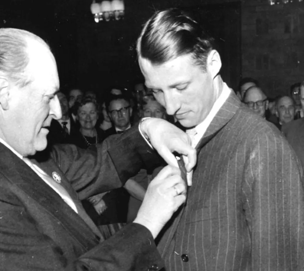 Foto i svart hvit av H.K.H. kronprins Harald utnevnes til æresmedlem i foreningen av æresmedlem H.M. kong Olav i 1962. H.M. Kong Olav setter medaljen på H.K.M Harald 