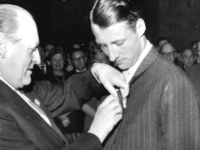 Foto i svart hvit av H.K.H. kronprins Harald utnevnes til æresmedlem i foreningen av æresmedlem H.M. kong Olav i 1962. H.M. Kong Olav setter medaljen på H.K.M Harald 