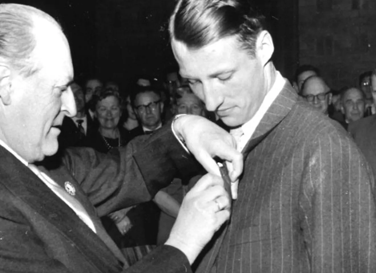Foto i svart hvit av H.K.H. kronprins Harald utnevnes til æresmedlem i foreningen av æresmedlem H.M. kong Olav i 1962. H.M. Kong Olav setter medaljen på H.K.M Harald