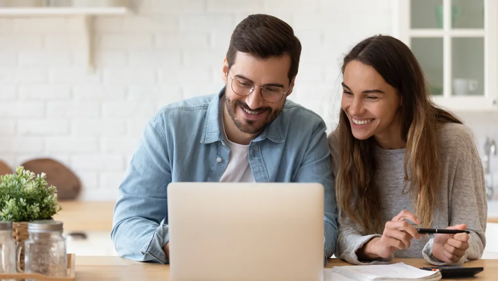 Ungt par foran laptop setter opp pensjonskonto og smiler