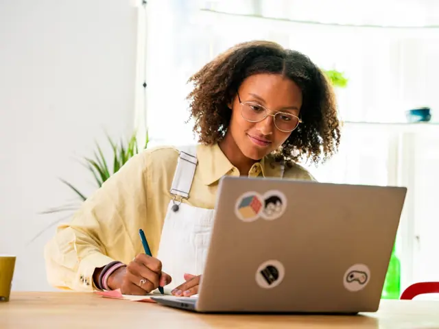 Ung kvinne noterer på papir og ser på en dataskjerm