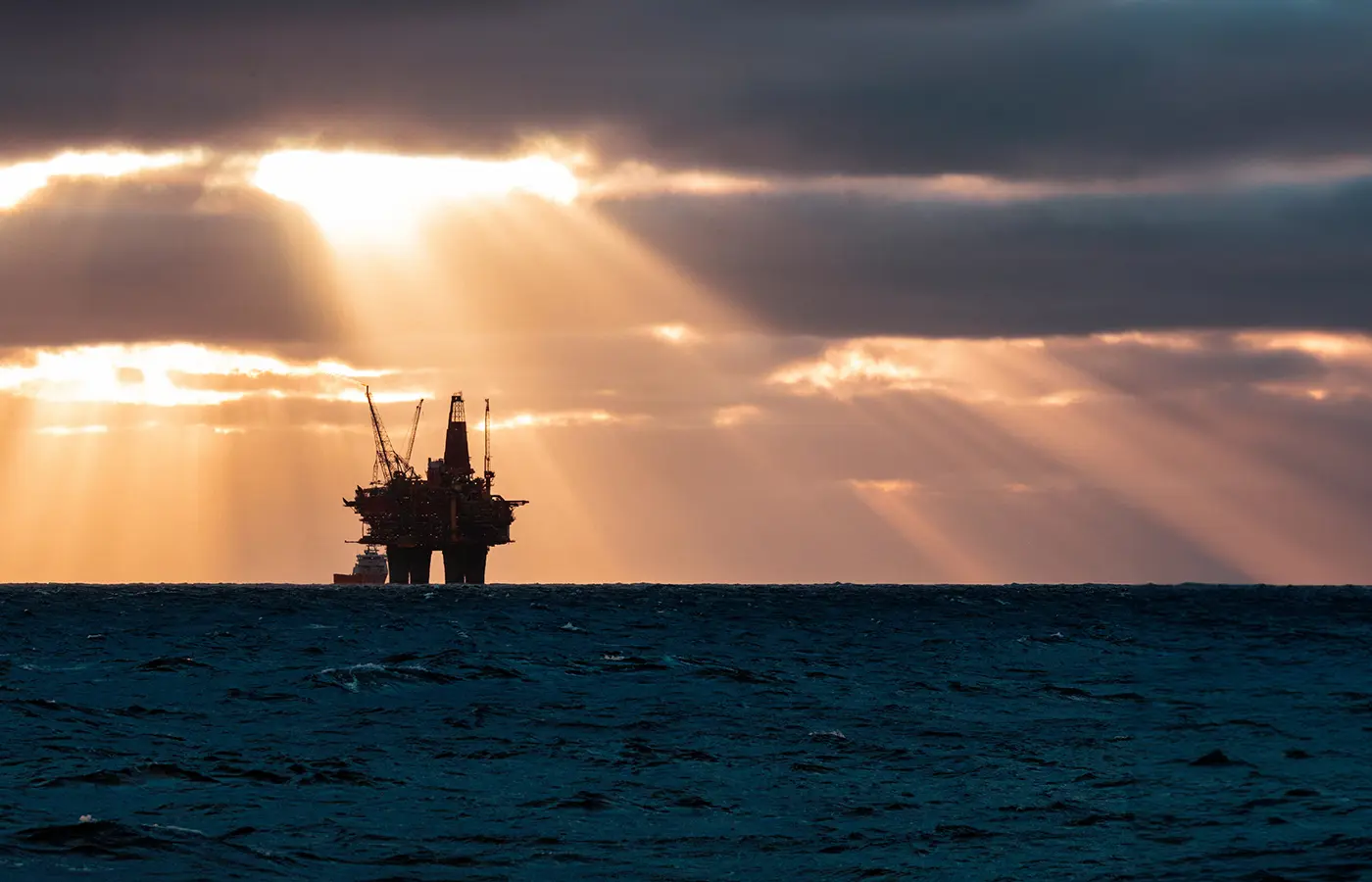 Offshore produksjonsplattform i Nordsjøen med dramatisk sollys gjennom skyene, symboliserer olje- og gassproduksjon og håndtering av produced water.