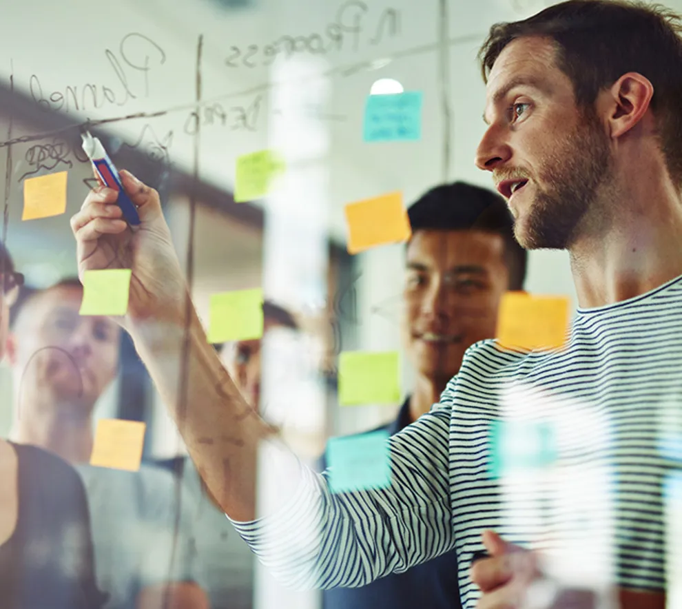 Gruppe diskuterer ideer og skriver på glassvegg med post-it-lapper.