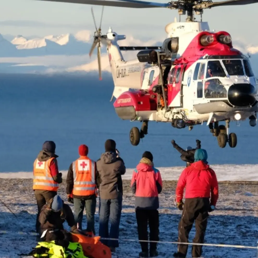 Redningshelikopter under øvelse med redningsmannskaper i snødekt landskap.