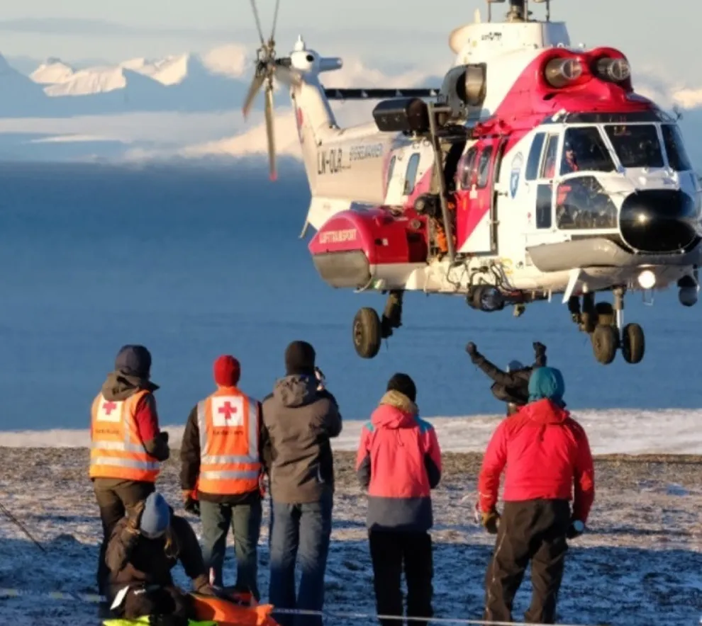 Redningshelikopter under øvelse med redningsmannskaper i snødekt landskap.