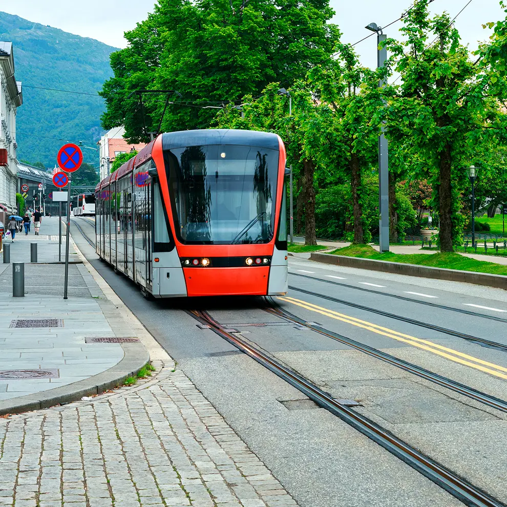 Bybanen i Bergen på skinner gjennom sentrum, omgitt av grønne trær og bymiljø.