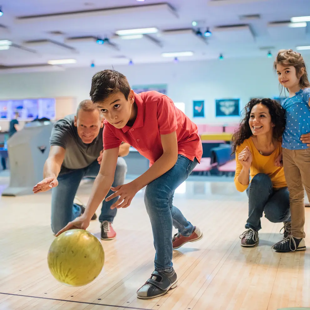 Familie spiller bowling sammen i bowlinghall med barn og voksne