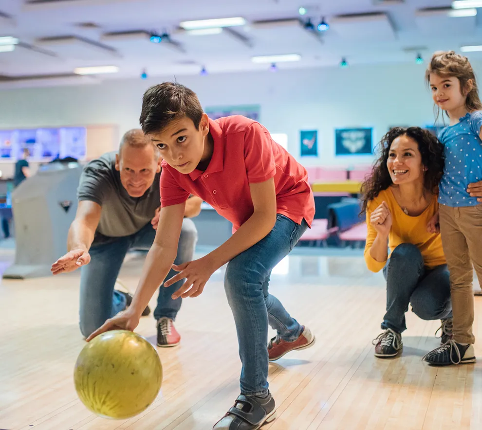Familie spiller bowling sammen i bowlinghall med barn og voksne