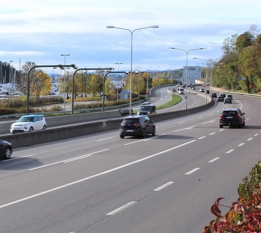 Biltrafikk på E18 med flere kjørefelt og veianlegg i urbane omgivelser.