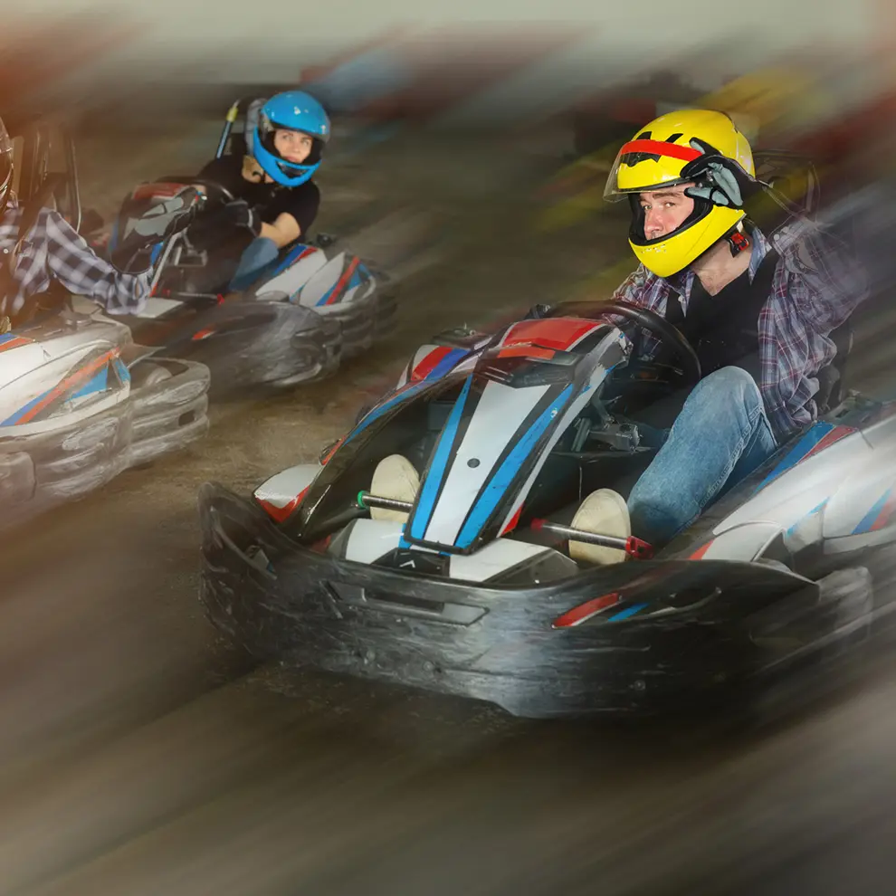 Gokartførere i full fart gjennom svingene på innendørs bane.