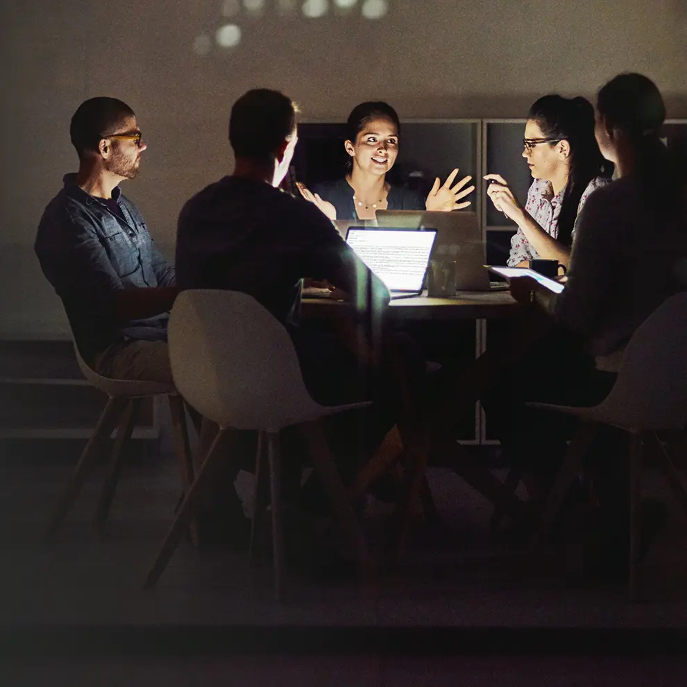 Gruppe utviklere i fokusert diskusjon rundt laptoper i et dempet rom