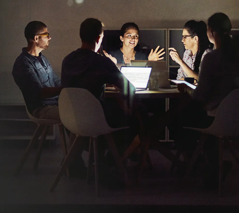 Gruppe utviklere i fokusert diskusjon rundt laptoper i et dempet rom