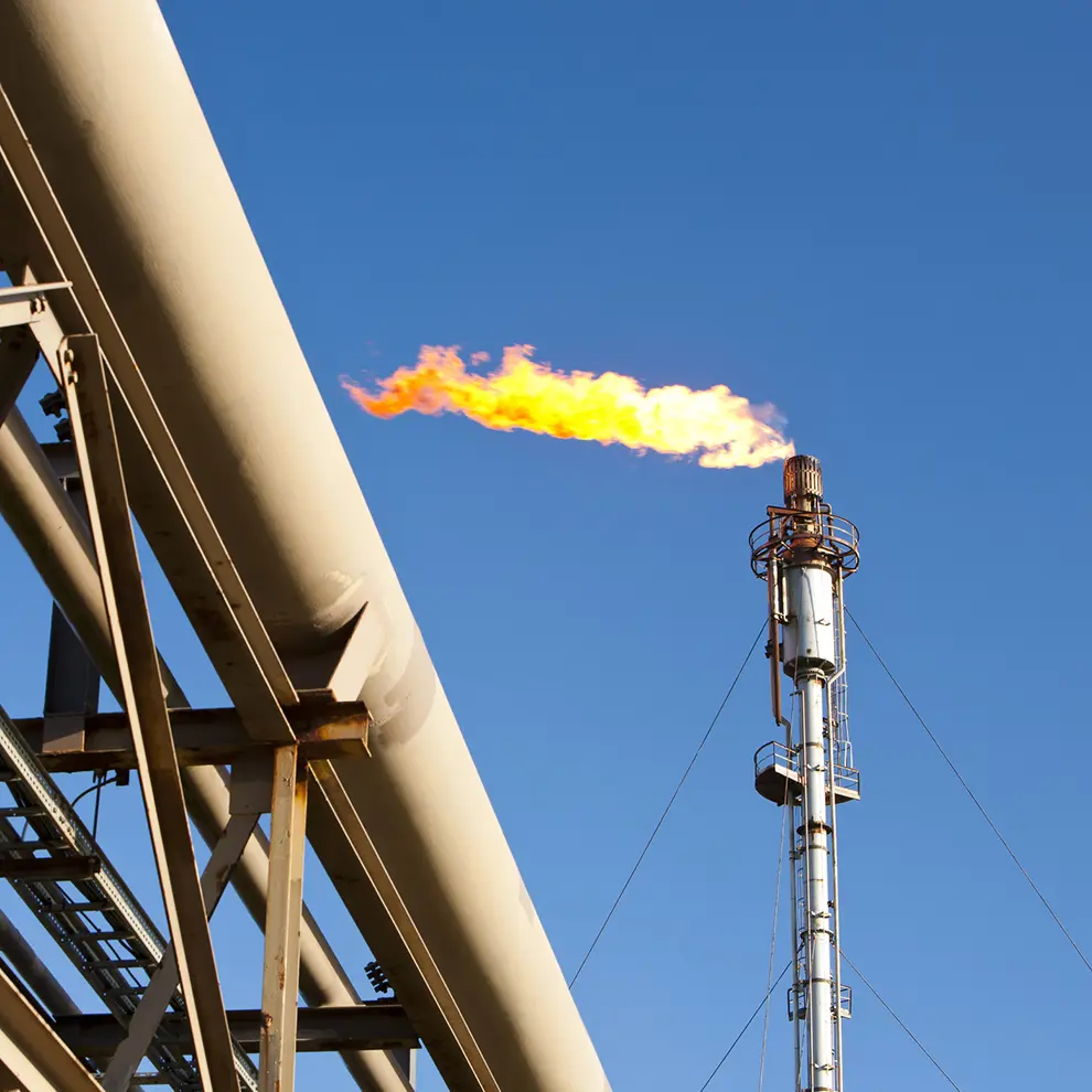 Gassfakkel og rørledning i olje- og gassanlegg under klar himmel