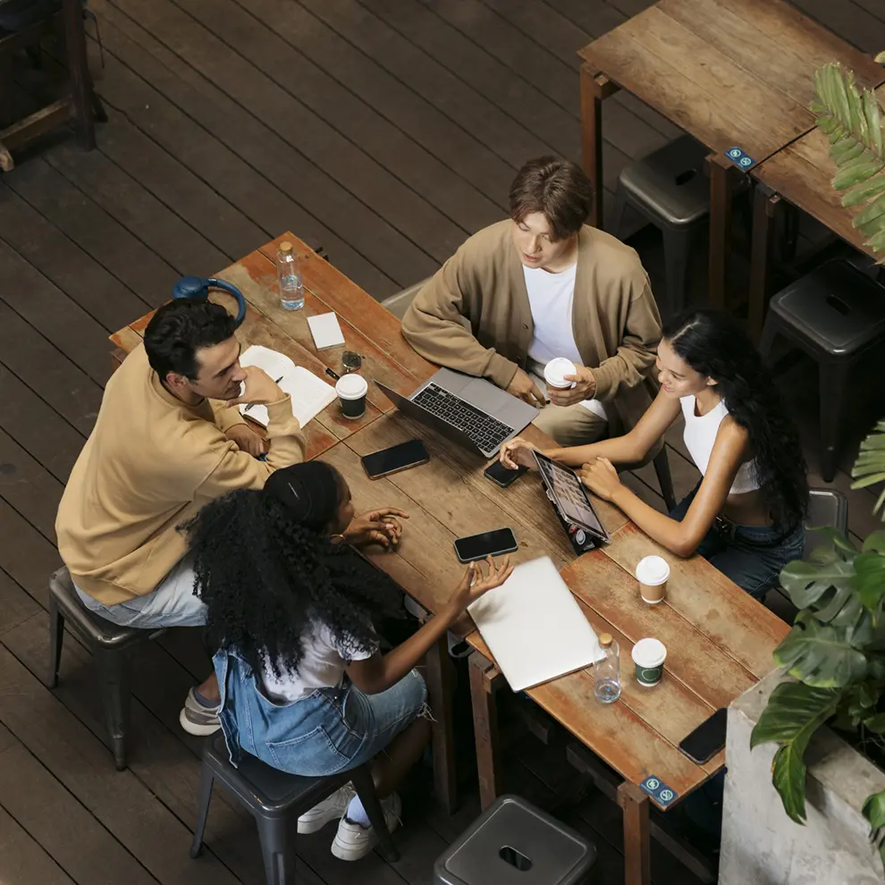 Gruppe unge utviklere diskuterer rundt bord med laptop og kaffe
