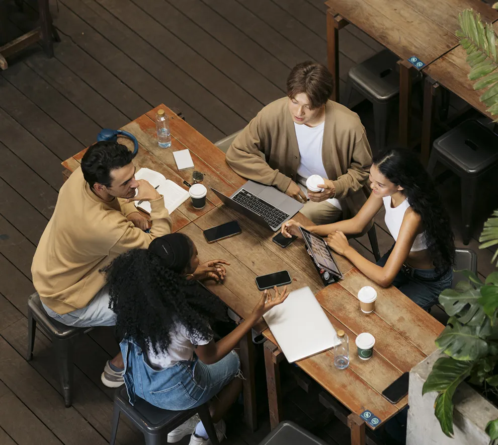 Gruppe unge utviklere diskuterer rundt bord med laptop og kaffe