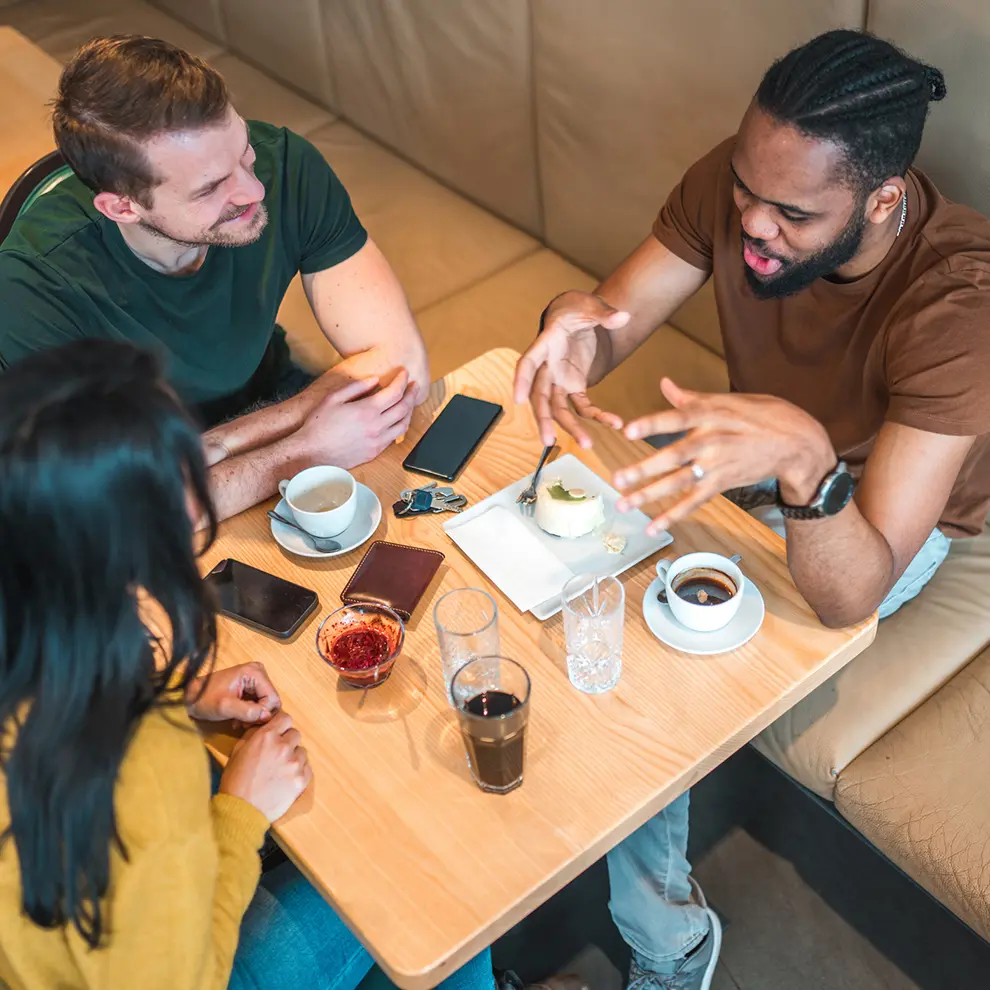 Tre personer i samtale over kaffe og mat på kafé