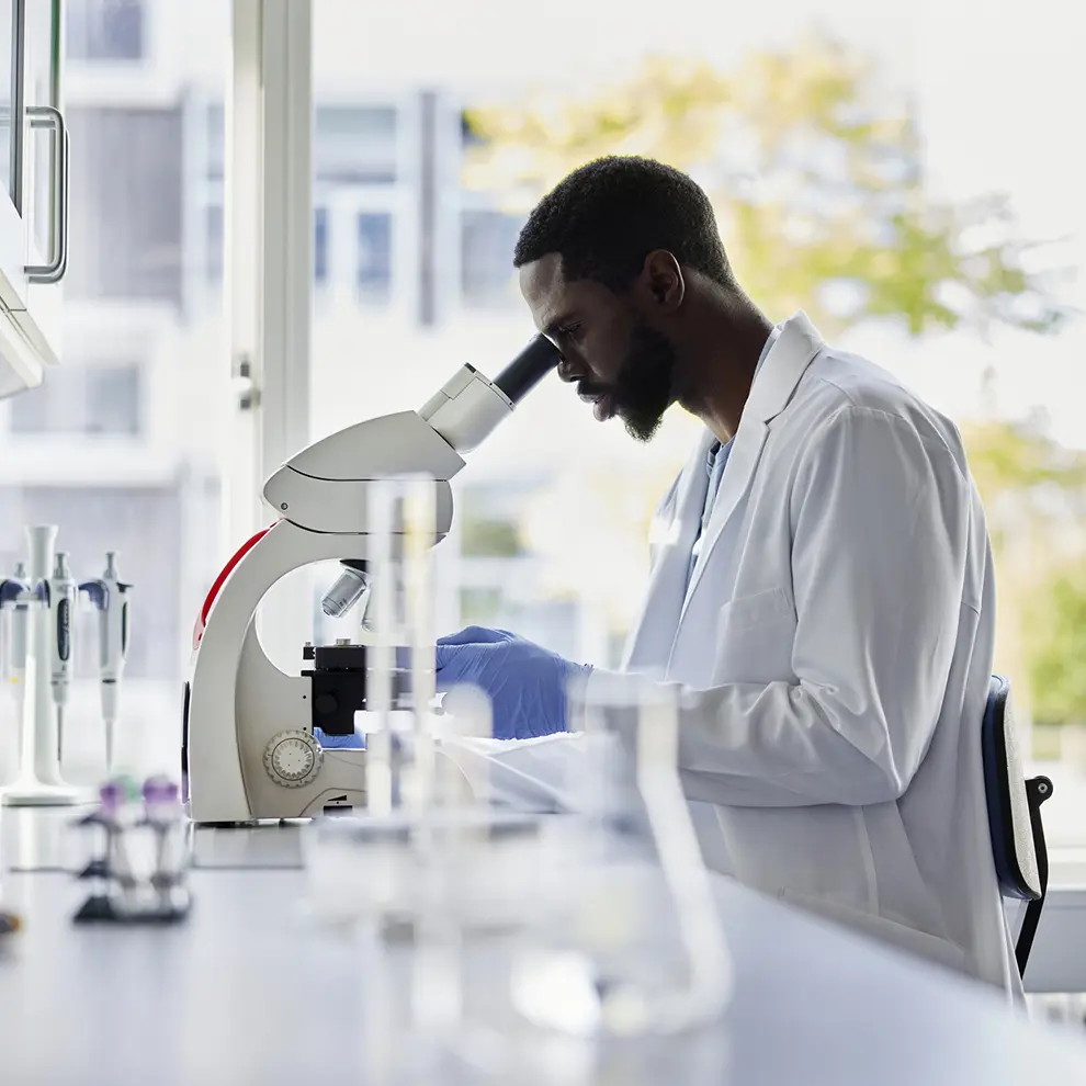 Forsker undersøker biologiske prøver i mikroskop på laboratorium.