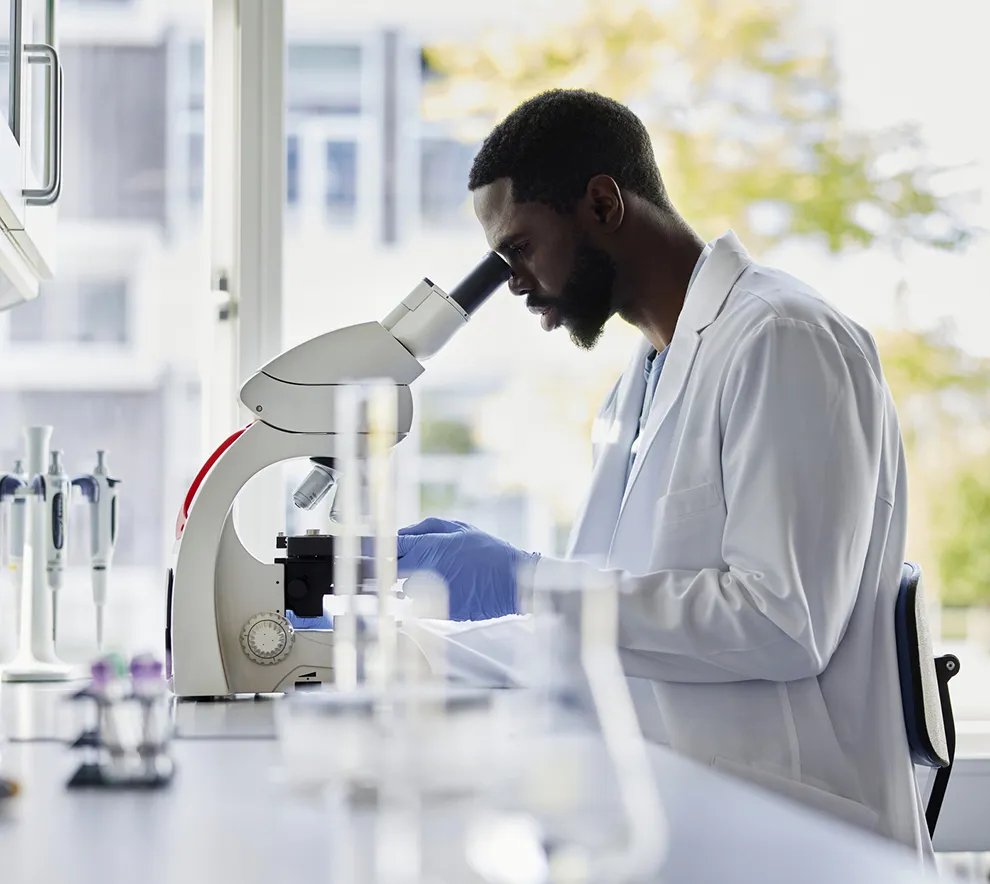 Forsker undersøker biologiske prøver i mikroskop på laboratorium.