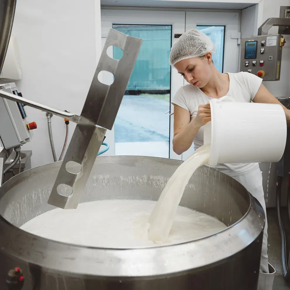Ansatt heller melk i en produksjonstank ved et meieri.