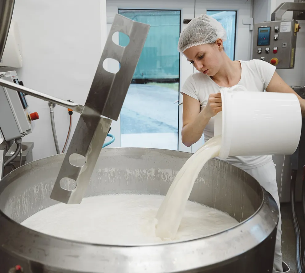 Ansatt heller melk i en produksjonstank ved et meieri.