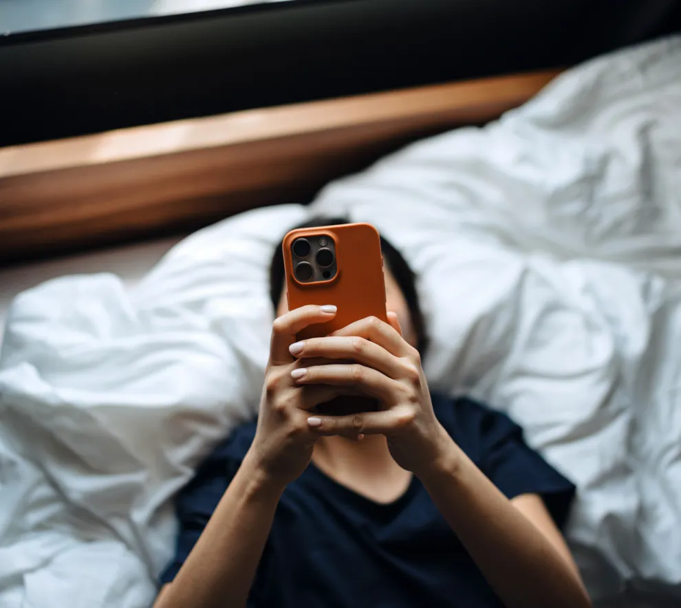 Person ligger i seng og bruker mobiltelefon, illustrerer mobilbruk og skjermtid