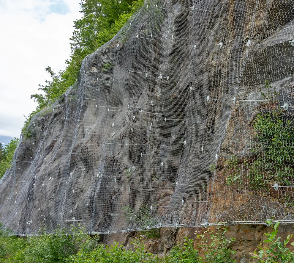 Rassikring med sikringsnett og fjellbolter på bratt fjellskråning for å hindre steinsprang og ras mot infrastruktur.
