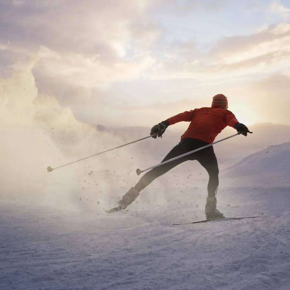 Langrennsløper som skøyter på ski i solnedgang over snødekt terreng.