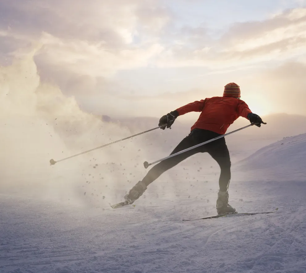 Langrennsløper som skøyter på ski i solnedgang over snødekt terreng.